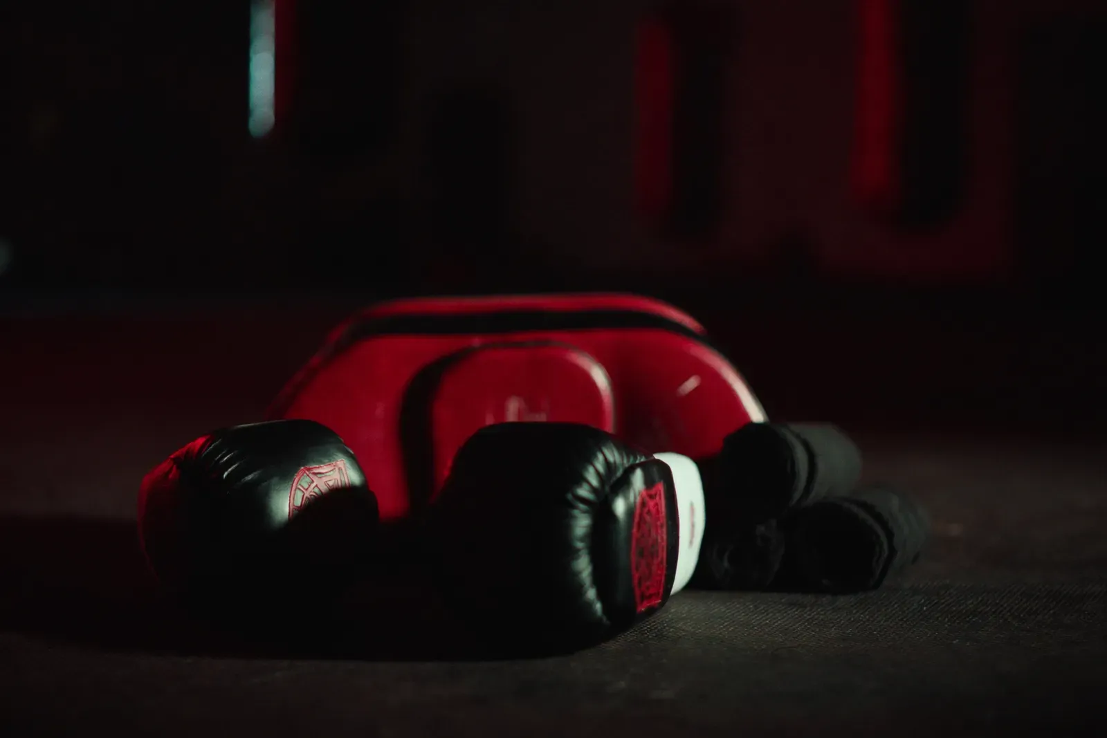 Red and black boxing gloves and a Thai kick pad on the mat, lit in dramatic red